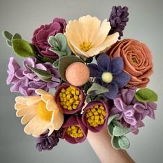 a hand holding a bouquet of flowers made out of felt and wool yarn, on a gray background