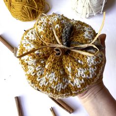 a hand is holding a small knitted pumpkin with twine and needles around it