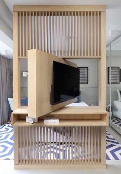 a flat screen tv sitting on top of a wooden shelf in front of a bed