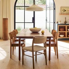 a dining room table with chairs and a bowl of fruit on the table in front of an arched window