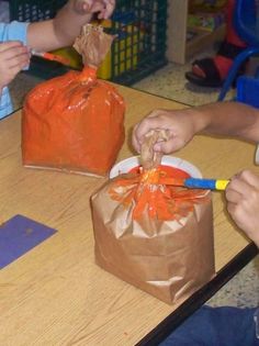 two children are sitting at a table and eating from plastic bags that have orange bows on them