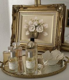 an ornate gold tray with perfume bottles and flowers on it in front of a framed painting