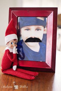 an elf is sitting next to a picture frame