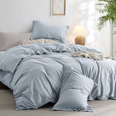 a bed with blue comforters and pillows in a room next to a potted plant