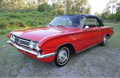 an old red car is parked in the grass