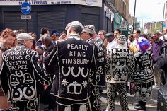 several people dressed in black and white clothing walking down the street with other people standing around