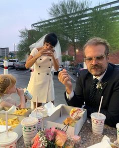 a man in a suit and tie sitting at a table with two children eating food