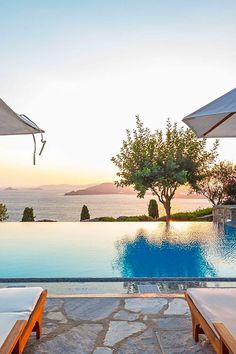 an outdoor swimming pool with lounge chairs and umbrellas overlooking the ocean at sunset or sunrise