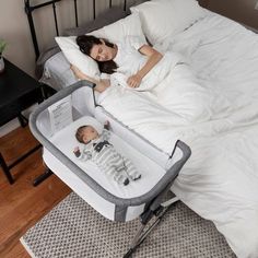 a woman laying in bed next to a baby sleeping on top of a crib