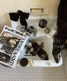 a bathroom sink filled with assorted shoes and other items next to a magazine on the floor