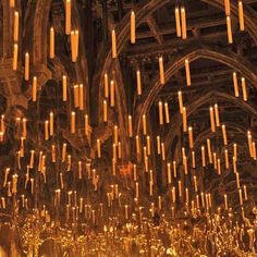 many lit candles are hanging from the ceiling in a building with arches and pillars that look like chandeliers