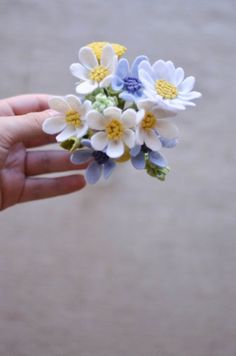 a hand holding a small bouquet of white, blue and yellow flowers on it's fingers