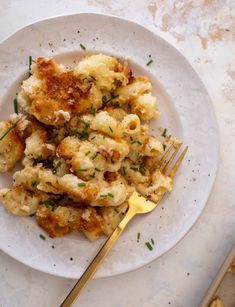 a white plate topped with macaroni and cheese covered in parsley next to a fork