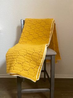 a yellow crocheted blanket sitting on top of a chair next to a wall