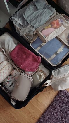 an open suitcase filled with clothes on top of a wooden floor next to a purple rug