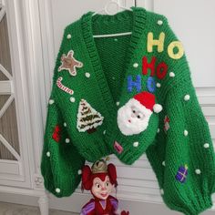 a green christmas sweater hanging on the wall next to a doll and toy figurine