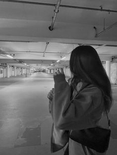 a woman standing in an empty parking garage holding her cell phone up to her ear