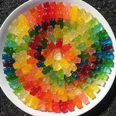 a white bowl filled with gummy bears on top of a black floor next to a sidewalk