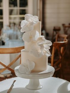 a wedding cake with white flowers on top sitting on a table in front of a window