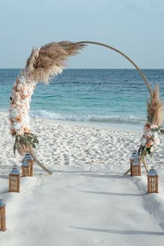 an arch decorated with flowers and feathers on the beach