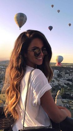 a woman sitting on top of a building with hot air balloons flying in the sky