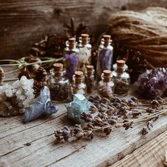 several bottles filled with different types of crystals and herbs on a wooden table next to twine of twine