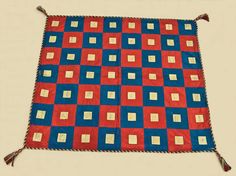 a red, blue and white quilt with tassels on it's edges