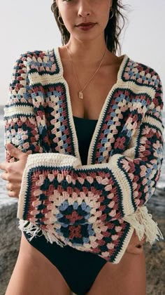 a woman in a bathing suit standing on the beach wearing a crocheted shawl