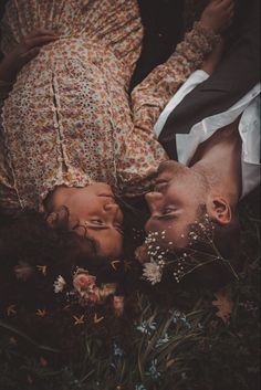 two people laying on the ground with flowers in their hair and one person wearing a dress