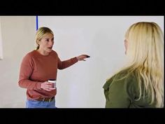 a woman standing in front of a whiteboard pointing to another woman who is holding a cup