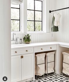 a kitchen with white cabinets and black and white tile flooring that has three bins in front of the sink