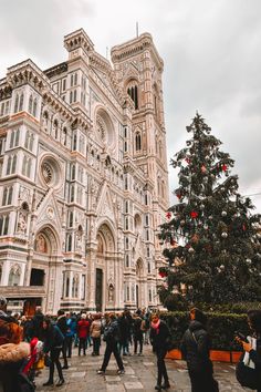 people are walking around in front of a large building with a christmas tree on the corner