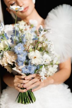 a woman in a wedding dress holding a bouquet of white and blue flowers with an angel nosepiece