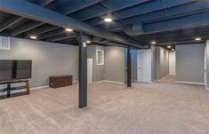 an empty living room with gray walls and ceiling beams, carpeted flooring and a flat screen tv mounted to the wall