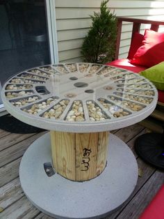 a table made out of wood and rocks on a deck with red cushions in the background