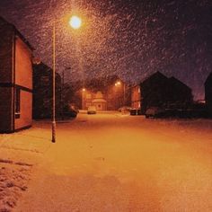 an empty street at night with snow falling on the ground and buildings in the background