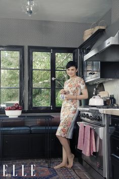 a woman standing in front of a window next to a stove top oven and sink