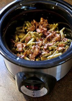 a crock pot filled with green beans and bacon sitting on top of a table