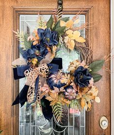 a wreath on the front door with blue flowers and greenery hanging from it's side