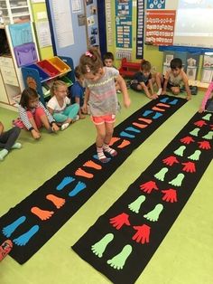 children sitting on the floor playing with black and green handprinted mats in a classroom