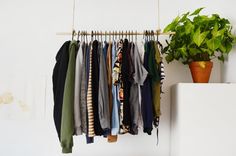 a bunch of clothes hanging on a rack next to a potted plant