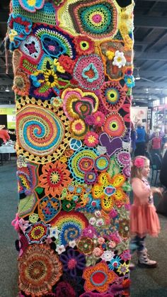 a large crocheted object is displayed in the middle of a room with people looking at it