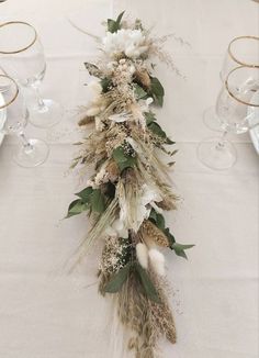 an arrangement of flowers and feathers on a table with wine glasses in the back ground