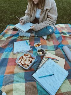 a woman is sitting on the grass with her notebook and food in front of her