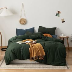 a bed with green comforter and pillows in a white room next to a lamp