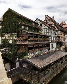 an old building with flowers growing on the side of it next to a body of water