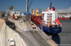 a large cargo ship in the water next to a train track with cars on it