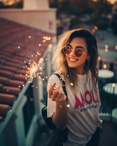 a woman with sunglasses and a t - shirt holding sparklers in front of her face