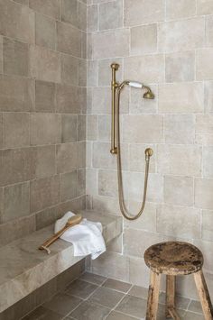 a walk in shower sitting next to a wooden stool on top of a tiled floor