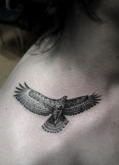 an owl tattoo on the back of a woman's upper chest, with wings spread out